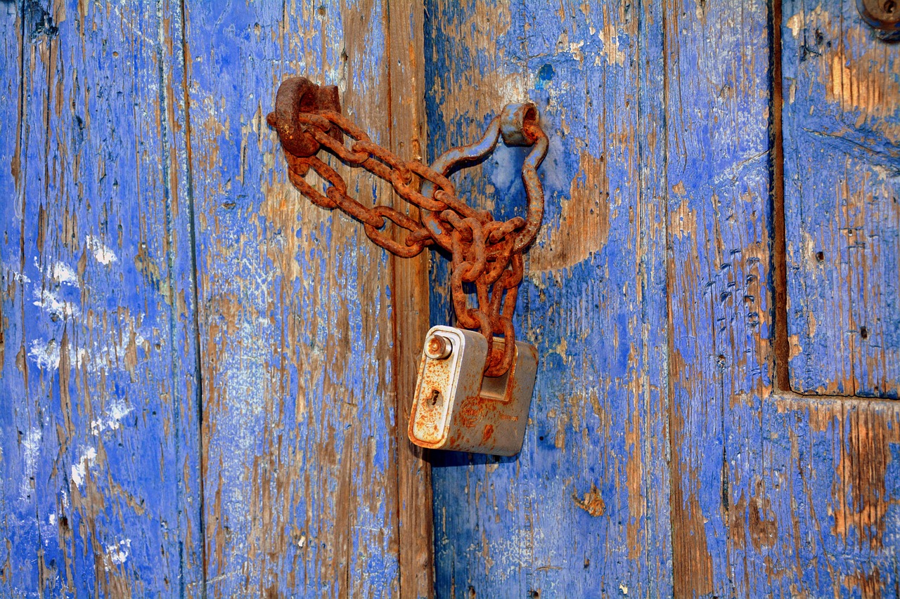 Rusty padlock chained to a blue door